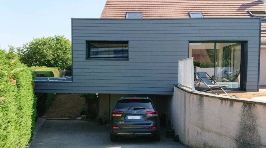Détail de l'extension moderne en ossature bois avec bardage gris foncé, montrant les finitions des menuiseries et les brise-soleil horizontaux.