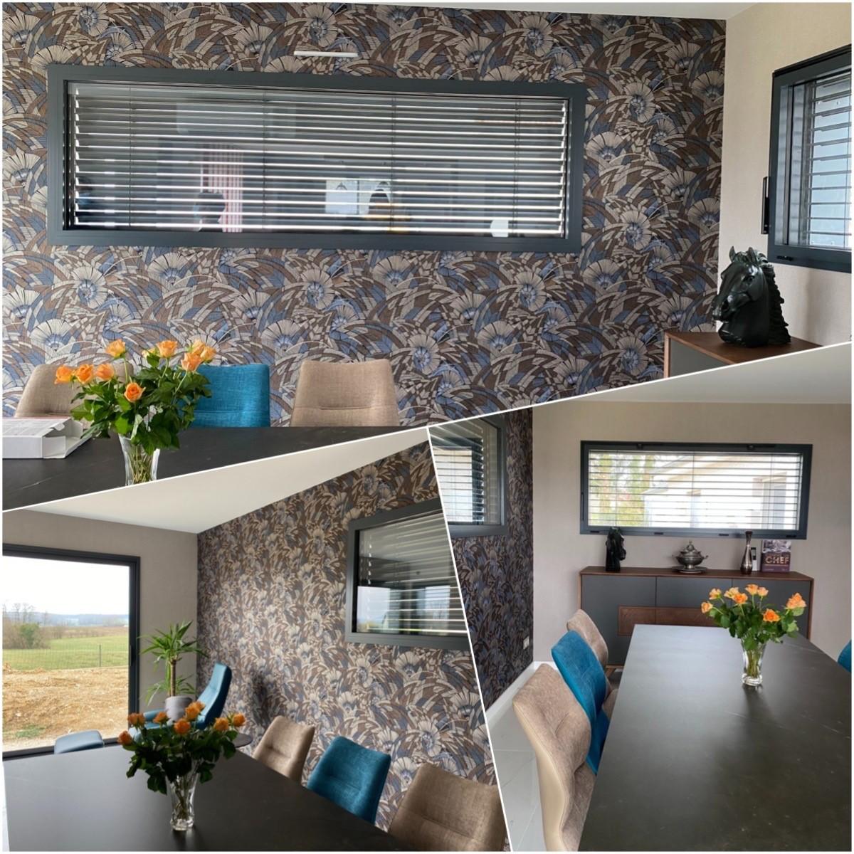 Aménagement intérieur d'une salle à manger lumineuse dans une extension en ossature bois, avec grandes fenêtres, brise-soleil orientables (BSO) et papier peint floral.
