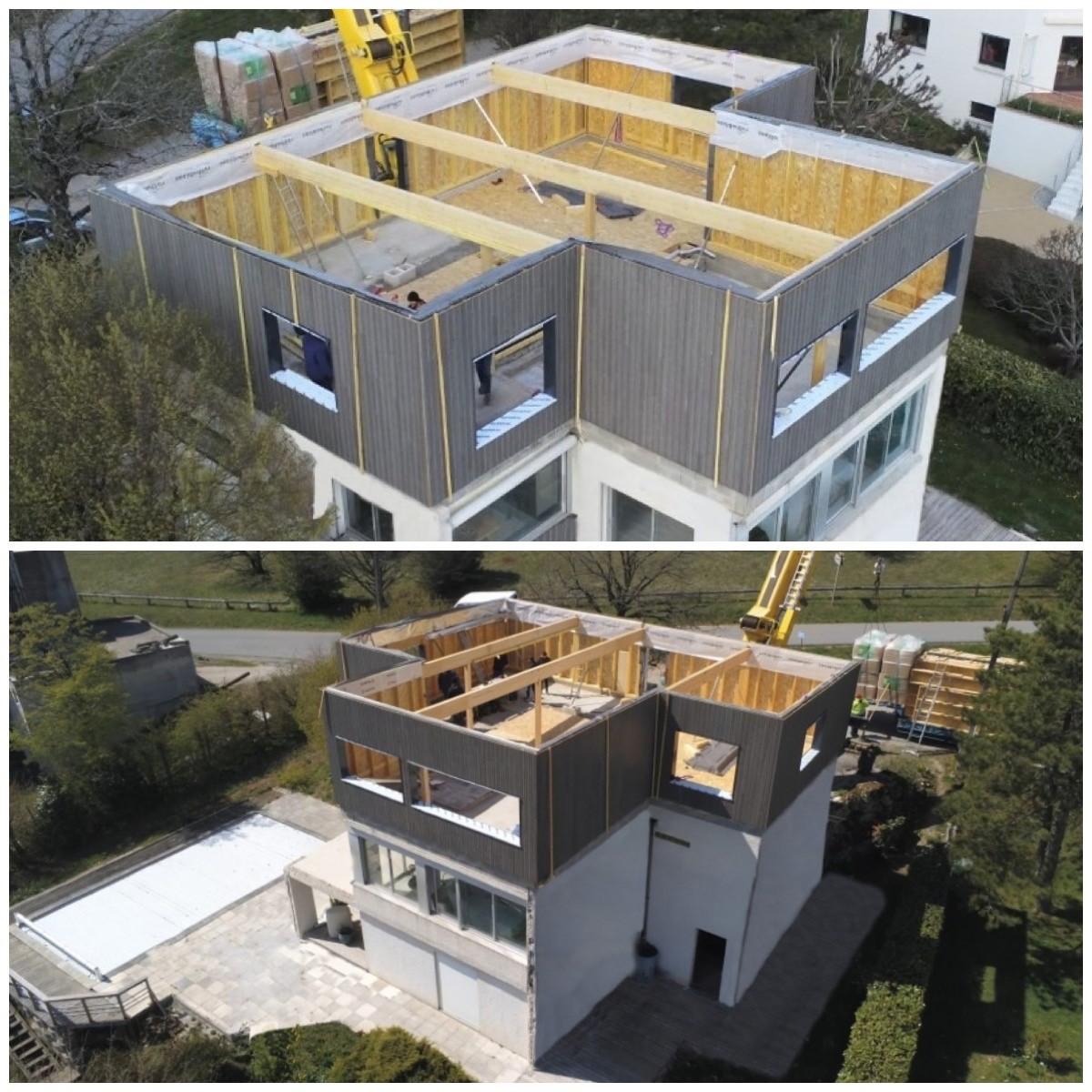 Vue aérienne d'une surélévation en ossature bois en cours de construction, montrant la nouvelle structure avec bardage gris ardoise, la charpente du toit plat et la grue de levage.