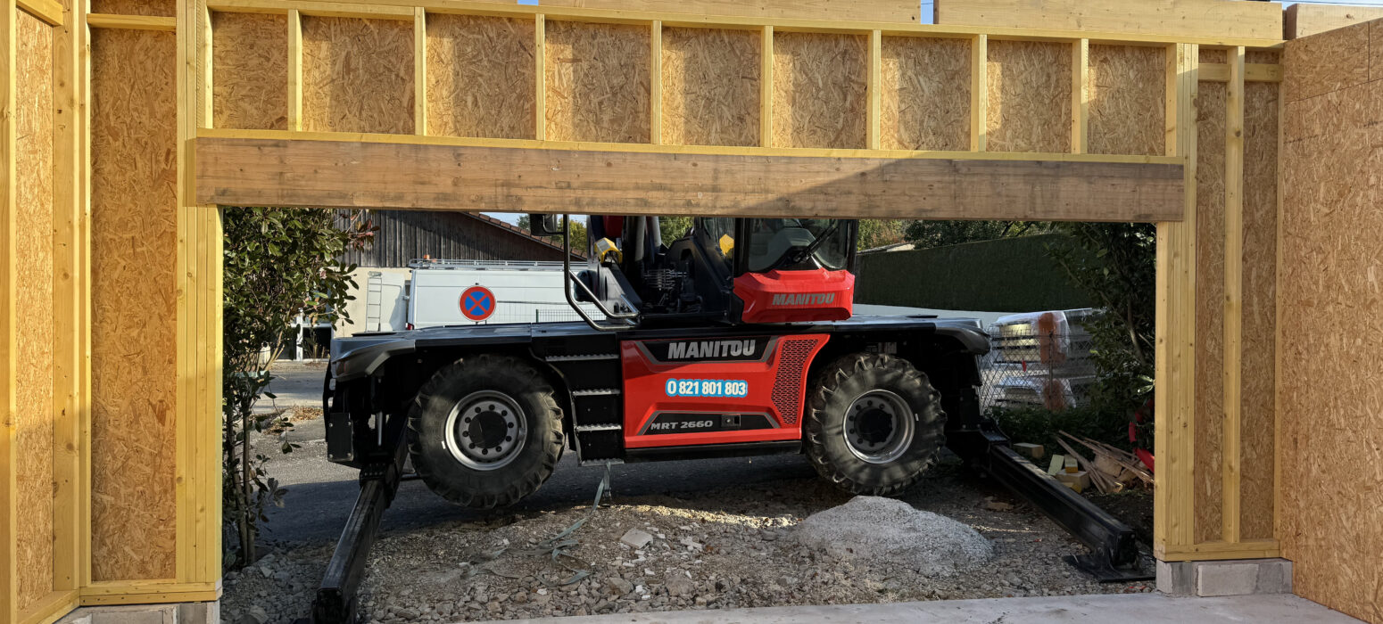 Engin de levage visible à travers la grande ouverture de porte de garage en ossature bois